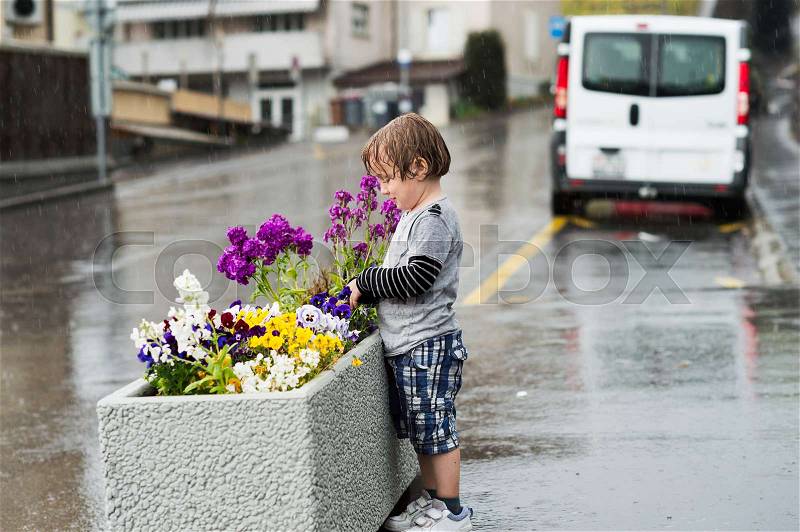 Cute little boy playing under the rain in a city, stock photo