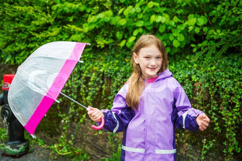 Pretty little girl under the rain, wearing purple rain coat, holding umbrella, stock photo