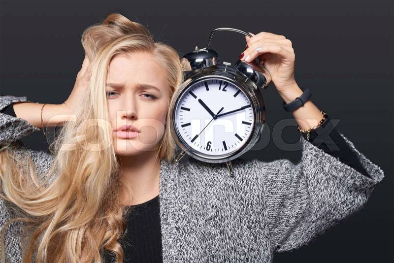Stressed woman holding big alarm clock over grey, stock photo