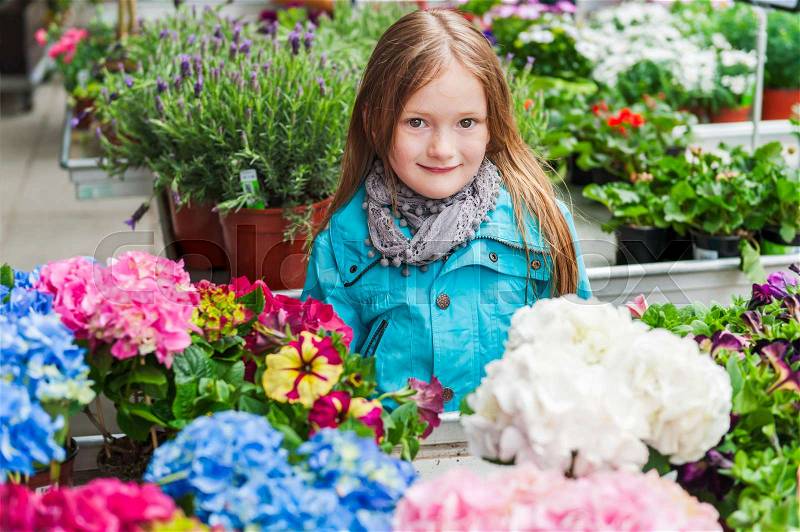 Spring portrait of a cute little girl choosing flowers in flower shop, stock photo