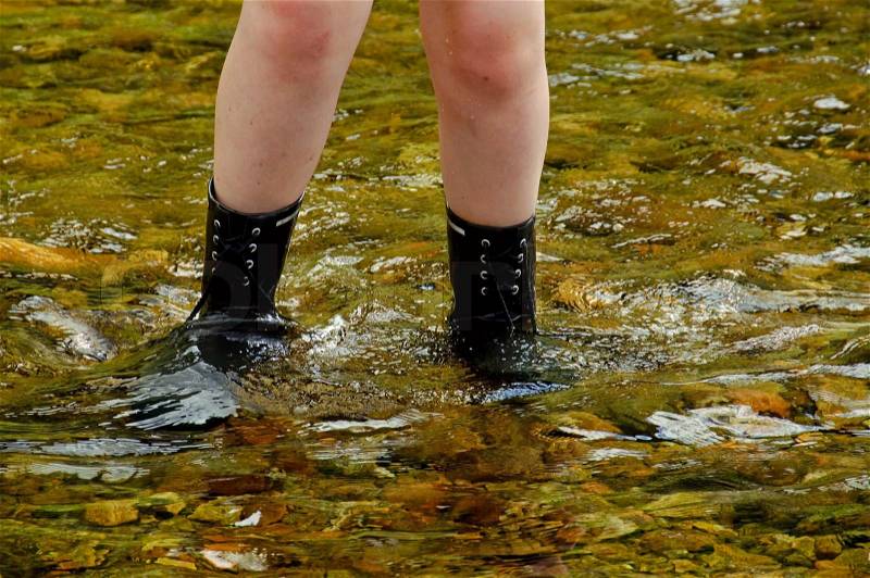 Close-up of a pair of legs in wellingtons crossing a river, stock photo