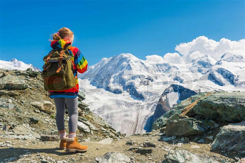 Cute little girl wearing backpack and colorful coat, standing in front of Gornergrat glacier, Switzerland, back view, stock photo