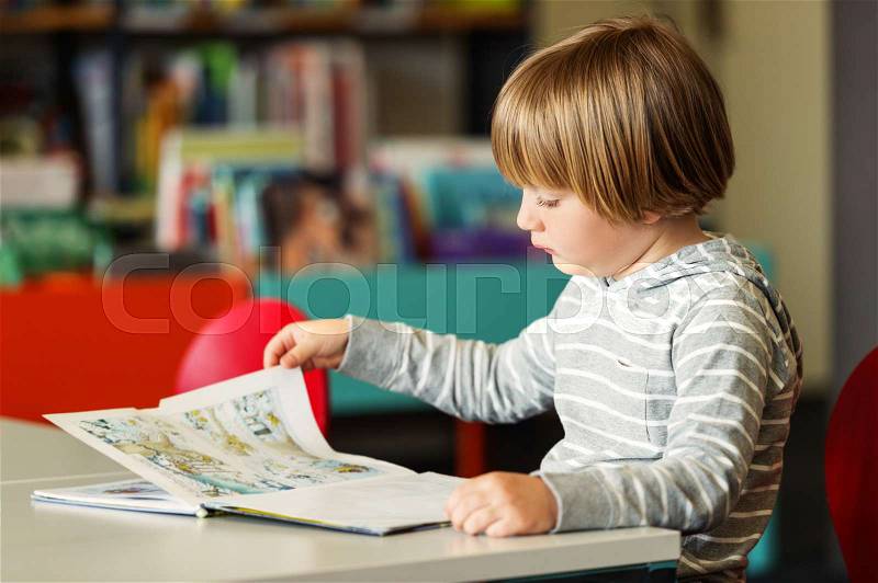 Little preschooler boy of 5 years old reading book in the library, stock photo