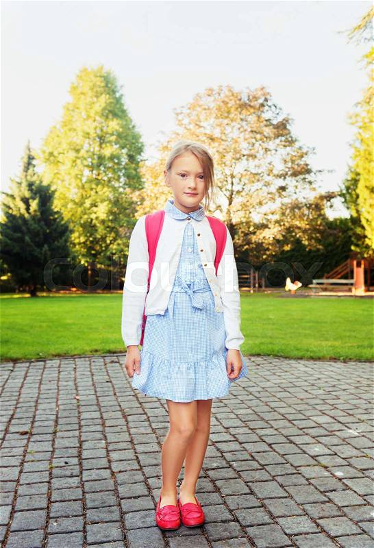 A young little girl preparing to walk to school, wearing blue mary jane dress and red moccasins, stock photo