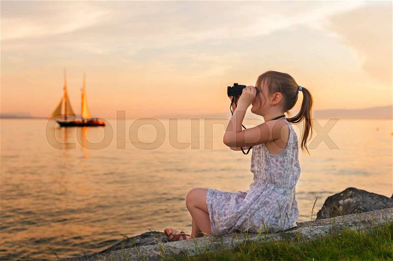 Outdoor portrait of a cute little girl playing by the lake on a nice warm evening, looking at the boat with binoculars, stock photo