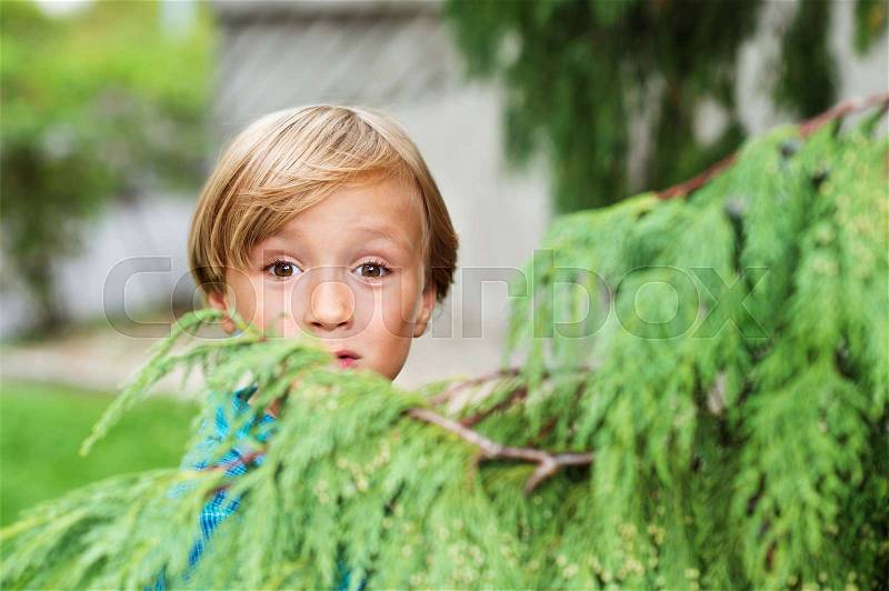 Outdoor portrait of a cute little boy on a nice sunny day, playing seek and find in the park, stock photo
