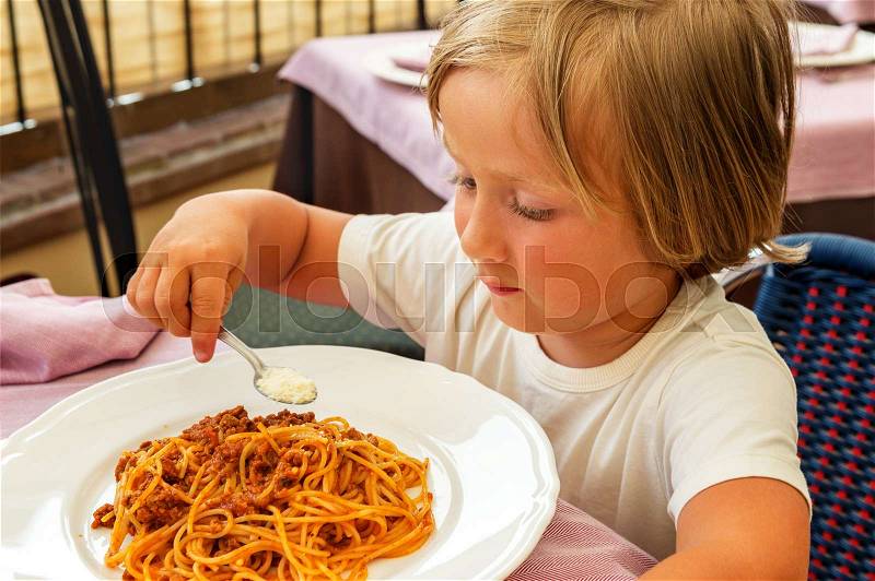 Adorable toddler boy eating spaghetti bolognese with cheese, stock photo