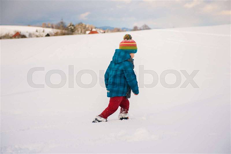 Cute little boy playing in snow field. Kid having fun outdoors, running on snow, wearing warm blue jacket, hat and scarf, stock photo