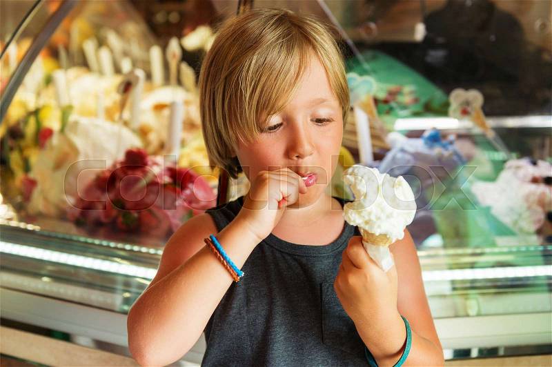 Cute toddler boy eating italian ice-cream in shop, stock photo