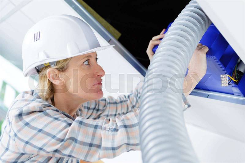 Female worker fitting ventilation system in buildings ceiling, stock photo