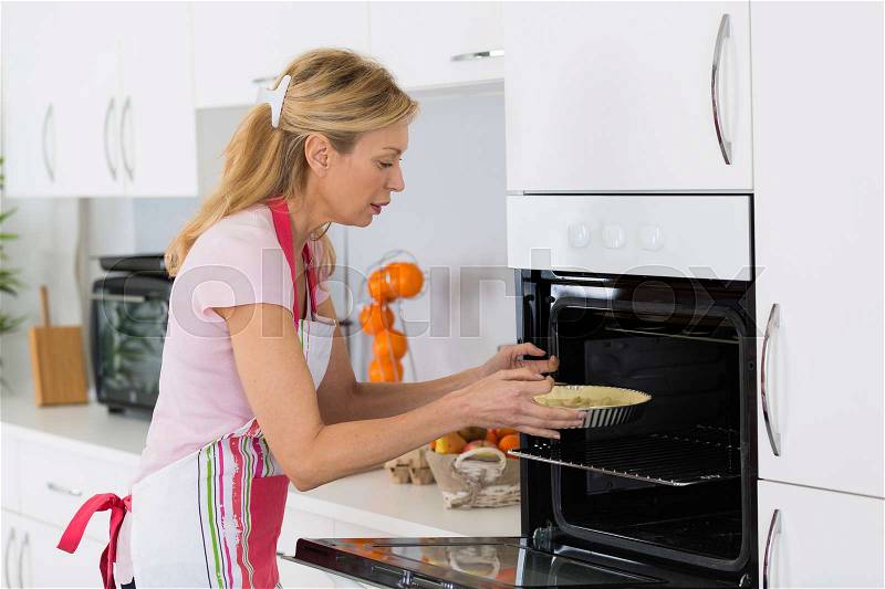 Woman doing baking placing a cake in the oven, stock photo