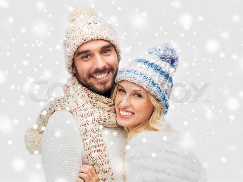 Winter, fashion, couple, christmas and people concept - smiling man and woman in hats and scarf hugging over snow background, stock photo