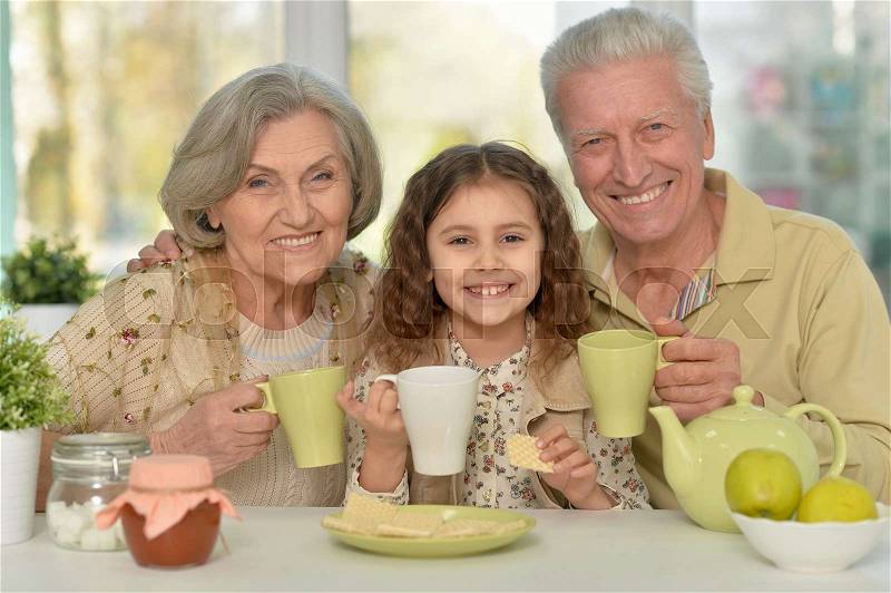 Grandparents with granddaughter drinking tea at home, stock photo