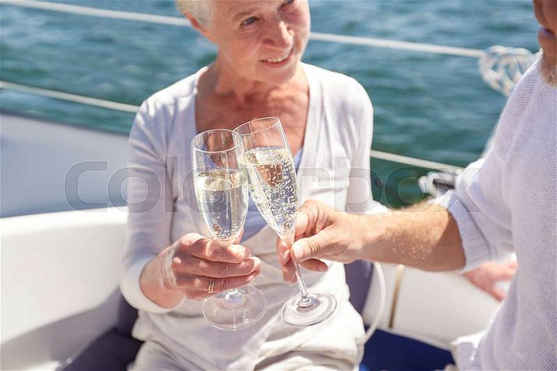 Sailing, age, travel, holidays and people concept - close up of happy senior couple drinking champagne on sail boat or yacht deck floating in sea, stock photo