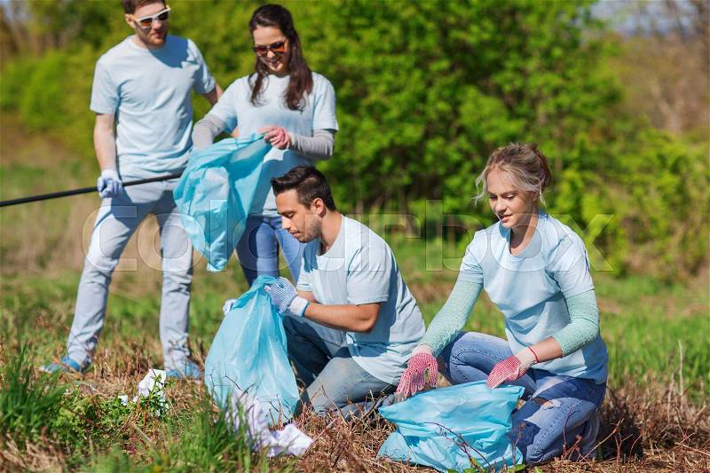 Volunteering, charity, cleaning, people and ecology concept - group of happy volunteers with garbage bags cleaning area in park, stock photo