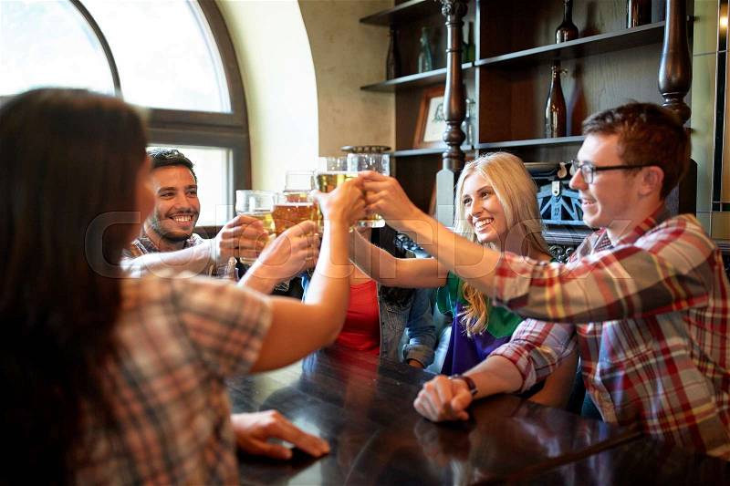 People, leisure, friendship and celebration concept - happy friends drinking draft beer and clinking glasses at bar or pub, stock photo