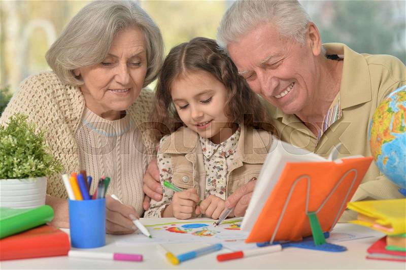 Portrait of a happy grandparents with granddaughter drawing together, stock photo