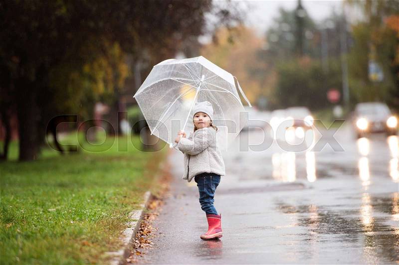 Cute little girl under the transparent umbrella in town on a rainy day, stock photo