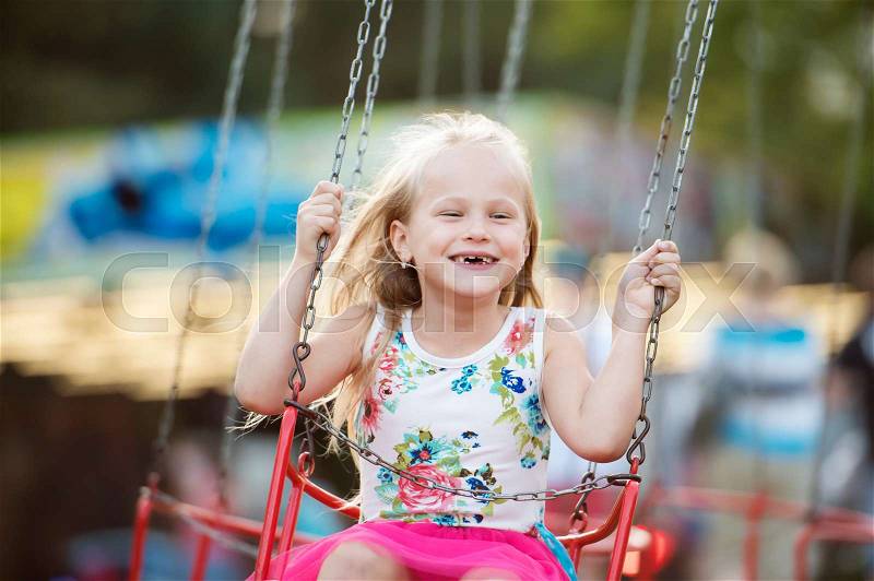 Cute little girl enjoing time at fun fair, chain swing ride, amusement park in summer, stock photo