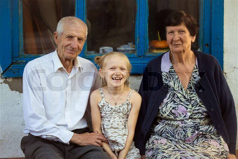 Granddaughter embracing with grand parents sitting at the front of rural house , stock photo
