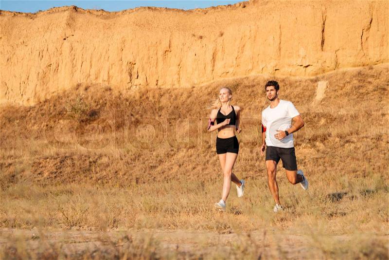 Athletic female runner and male fitness model running together outdoors, stock photo