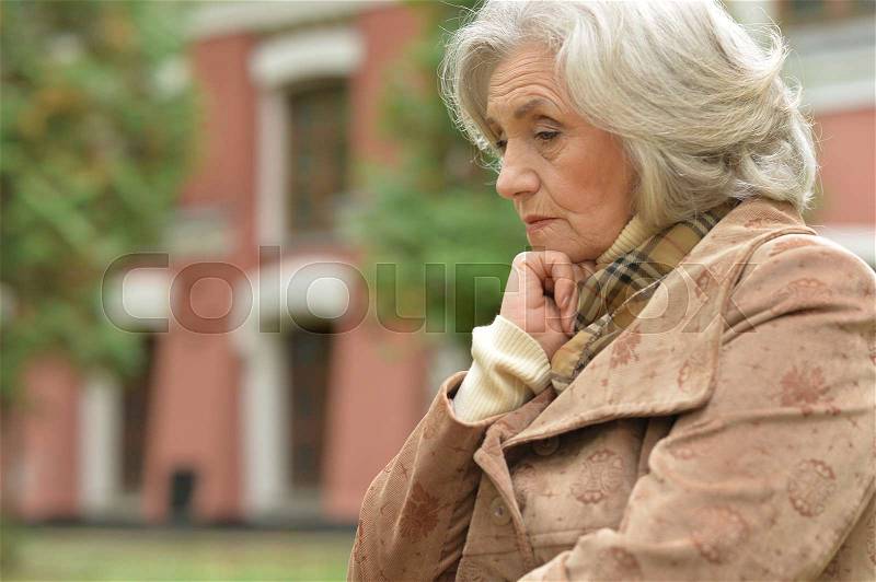 Sad elderly woman in autumn park, stock photo