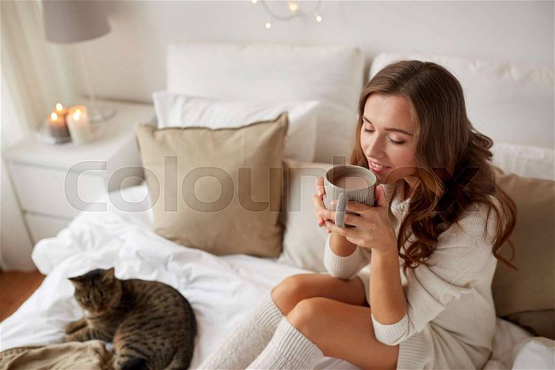 Morning, leisure, christmas, winter and people concept - happy young woman with cup of coffee or tea in bed at home bedroom, stock photo