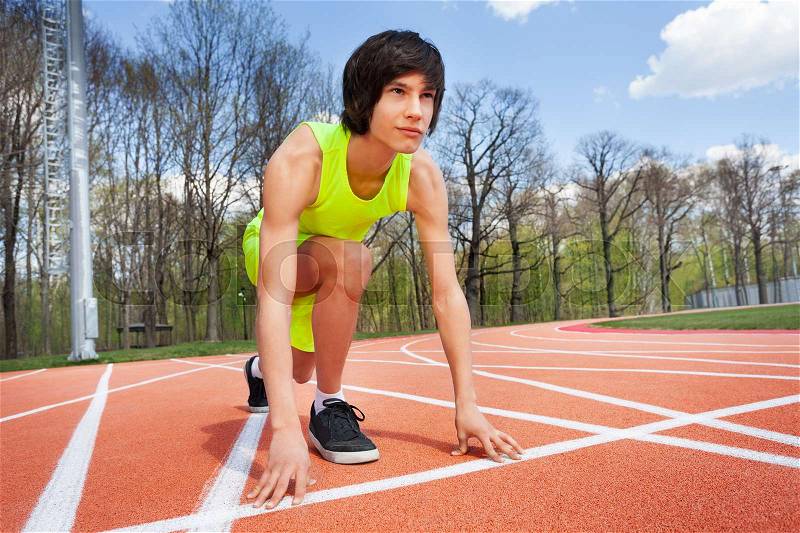 Portrait of teenage runner in start position, kneeling with hands on the line, ready to race on stadium, stock photo