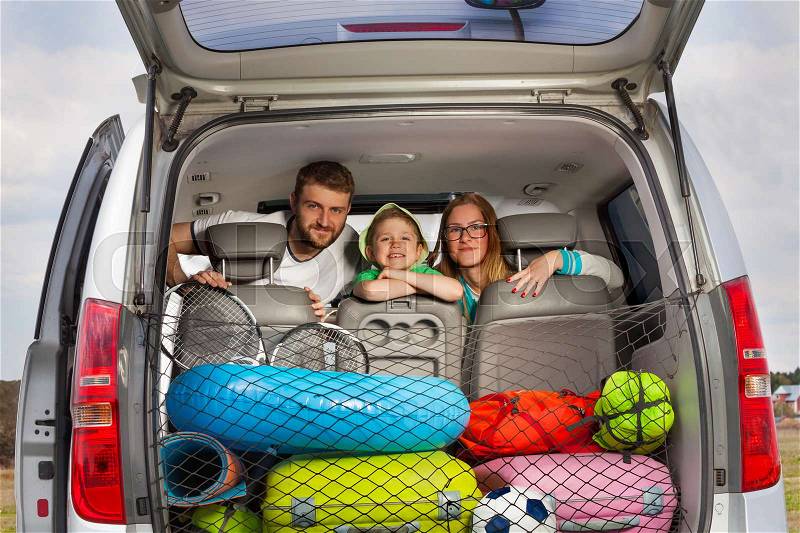 Happy young parents with their five years old son, sitting in their minivan, view from the car boot full of luggage, stock photo