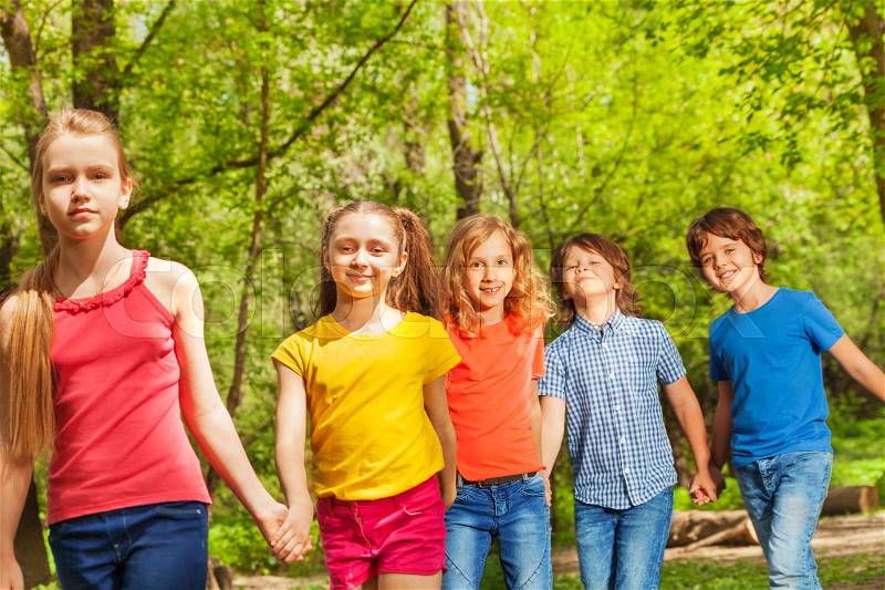 Portrait of five happy friends, ten years old boys and girls, walking in the park one by one holding hands, stock photo
