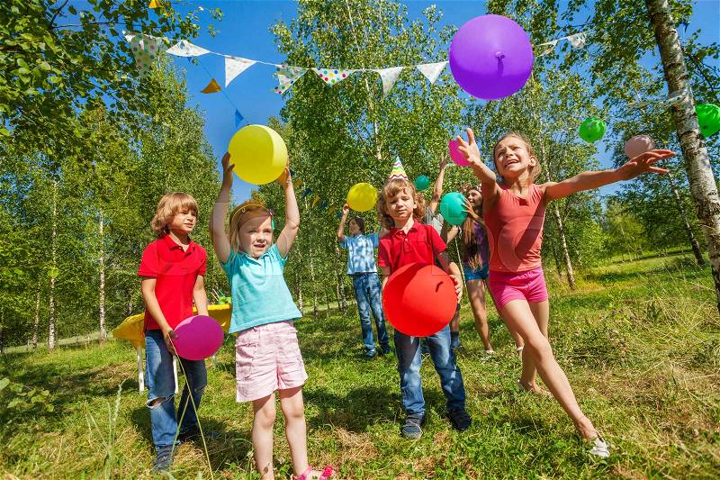 Happy little kids playing funny game with colorful balloons outside in summer, stock photo