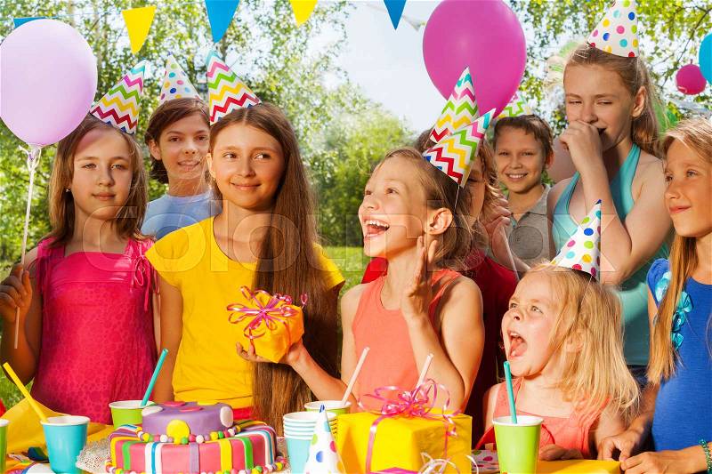 Group of happy kids congratulating excited girl at the outdoor birthday party, stock photo
