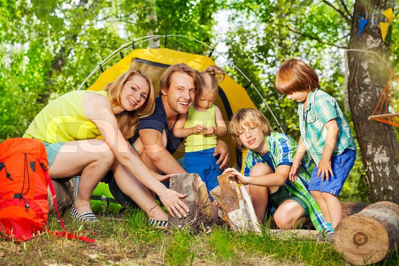 Happy young family, parents with three kids, making camp fire in the woods in summer, stock photo