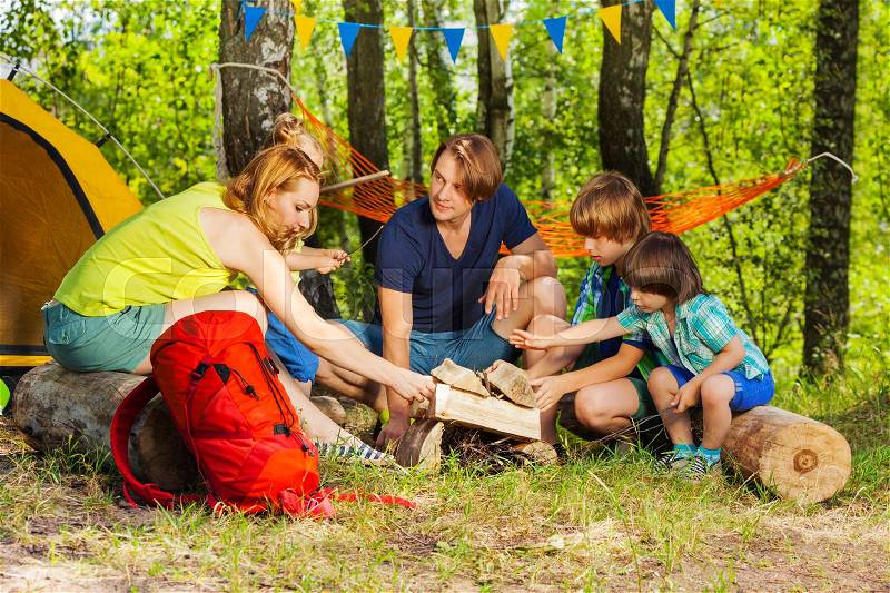 Happy young family, parents and kids, making camp fire with the fireplace log pieces in the woods, stock photo