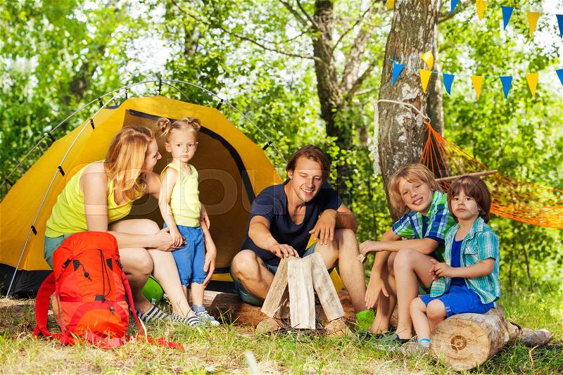 Active young family, parents and three kids, making camp fire with the fireplace log pieces in the woods, stock photo