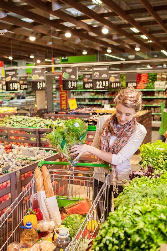 Portrait of beautiful young woman choosing green leafy vegetables in grocery store. Concept of healthy food shopping, stock photo