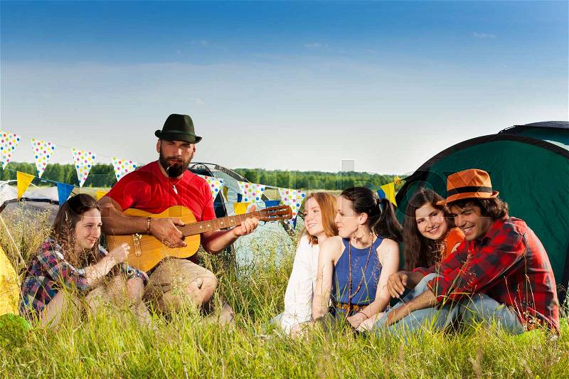 Laughing group of young people enjoying music of guitar on camping trip, stock photo