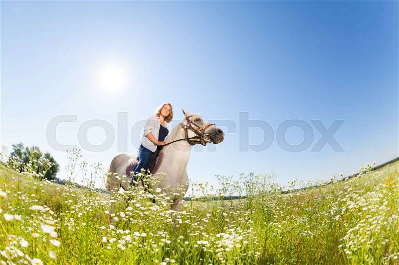 Portrait of pretty woman horseriding in the flowery meadow at sunny day, stock photo