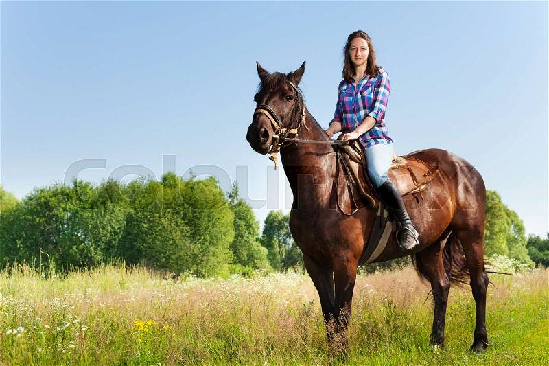 Portrait of female equestrian riding beautiful bay horse in summer, side view, stock photo