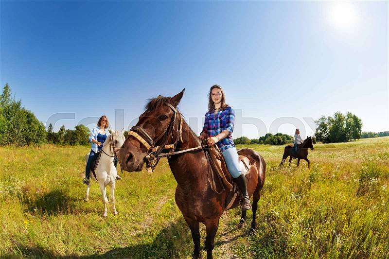 Three young female equestrians riding beautiful horses in flowery meadow, stock photo