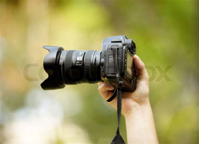 Hand of man with black professional camera, natural light, selective focus on nearest part, stock photo