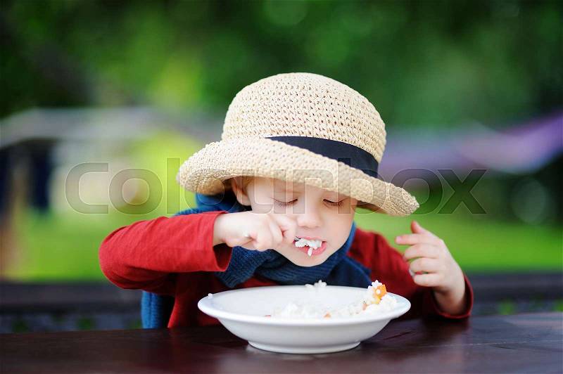 Cute toddler boy eating rice cereal outdoors. Healthy food for little kids, stock photo
