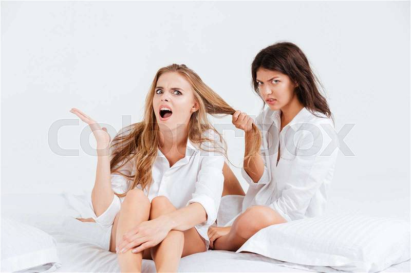 Two angry women in white shirt fighting while sitting in bed, stock photo