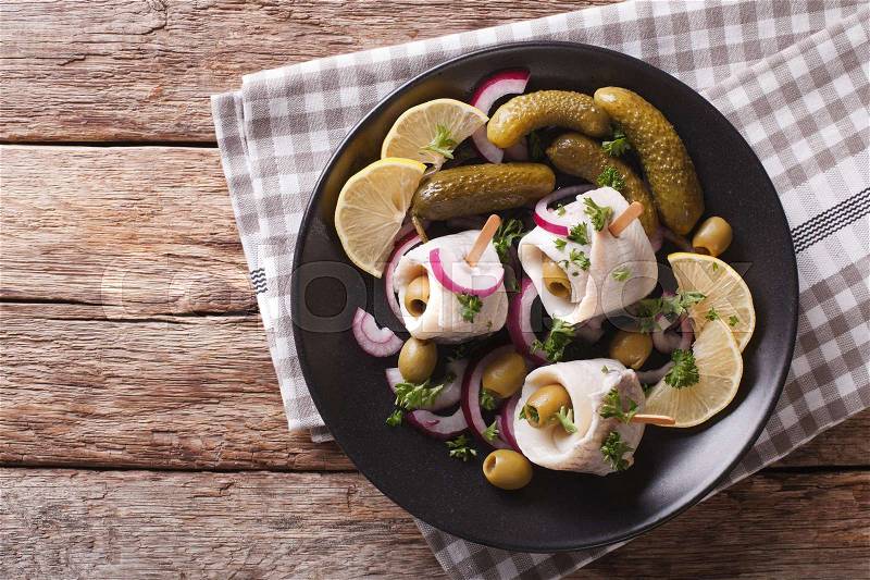 Rolls of marinated herring with olives, onions, pickles and lemon close-up on a plate on the table. Horizontal view from above , stock photo