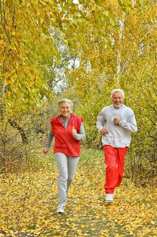 Happy fit senior couple exercising in autumn park, stock photo