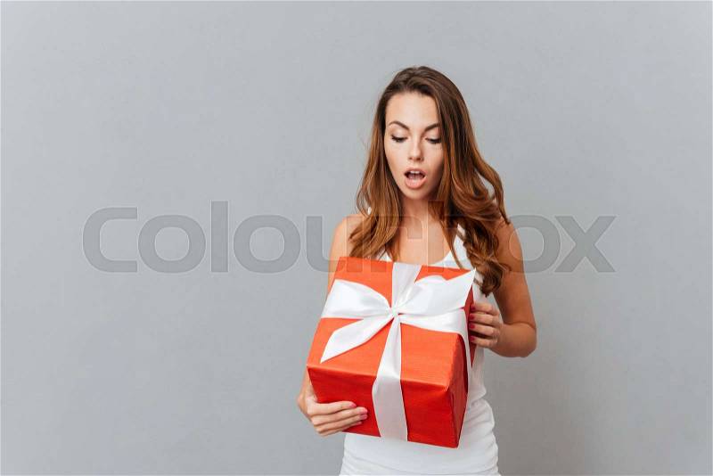 Cute surprised young woman open present box isolated on a gray background, stock photo