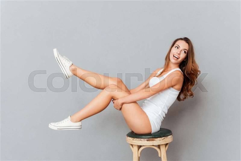 Laughing woman sitting on the chair with raised legs over gray backgorund, stock photo