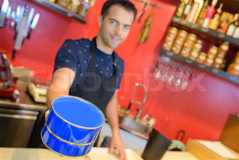 Man in deli holding blue tin, stock photo