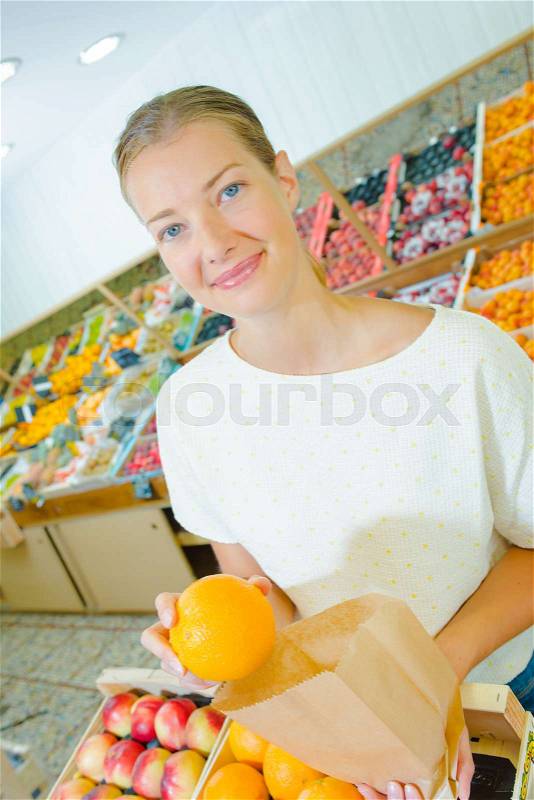 Young woman putting an orange in a paper bag, stock photo