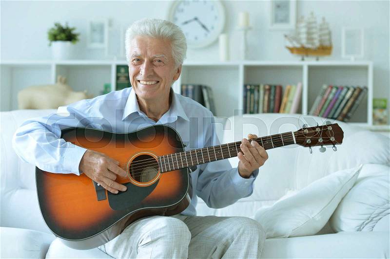 Happy senior man with guitar sitting on the sofa at home, stock photo